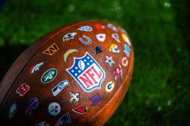 NEW YORK, USA, SEPTEMBER 11, 2023: NFL football ball, logo of national football league and logos of all teams. Green background, edit space clipart