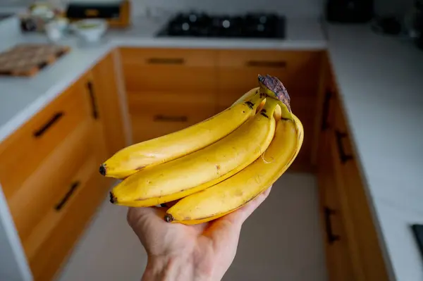 Man\'s hand holding bananas, natural daylight in the wooden kitchen