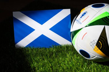 HAMBURG, GERMANY, APRIL 17, 2024: Scotland national flag and official soccer ball of Euro 2024 football tournament in Germany placed on green grass. Black background, edit space clipart