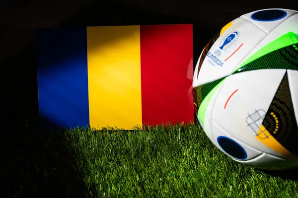 stock image MUNICH, GERMANY, APRIL 17, 2024: Romania national flag and official soccer ball of Euro 2024 football tournament in Germany placed on green grass. Black background, edit space