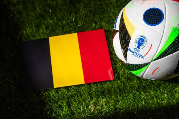 stock image MUNICH, GERMANY, APRIL 17, 2024: Belgium national flag and official soccer ball of Euro 2024 football tournament in Germany placed on green grass. Black background, edit space