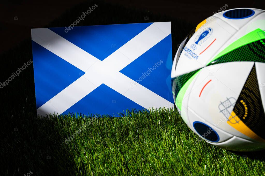 HAMBURG, GERMANY, APRIL 17, 2024: Scotland national flag and official soccer ball of Euro 2024 football tournament in Germany placed on green grass. Black background, edit space