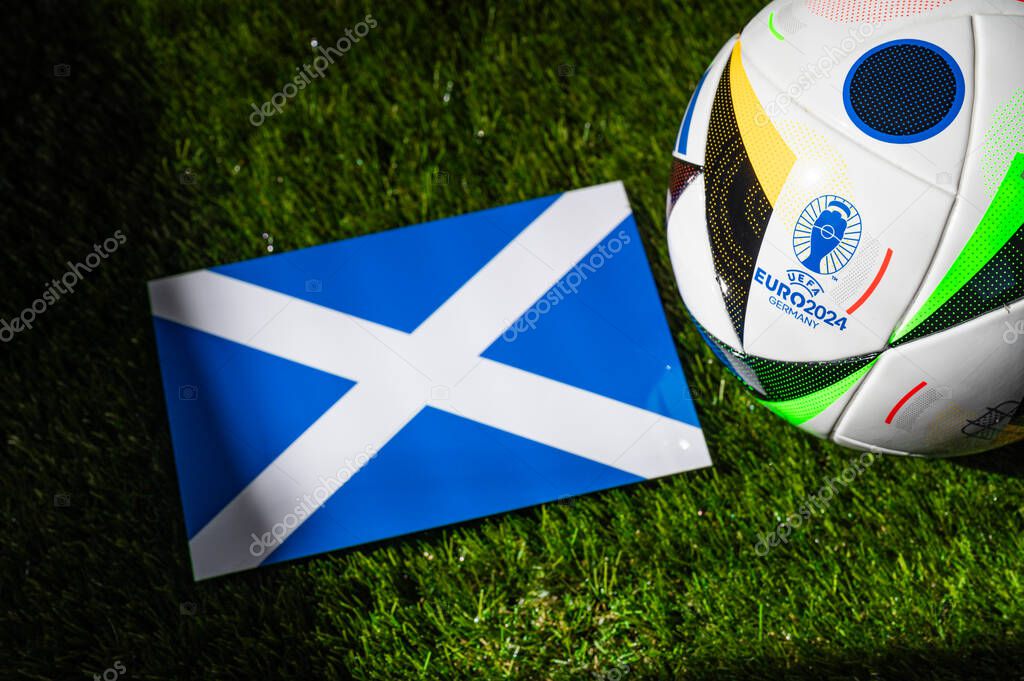 MUNICH, GERMANY, APRIL 17, 2024: Scotland national flag and official soccer ball of Euro 2024 football tournament in Germany placed on green grass. Black background, edit space