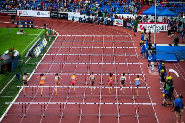 OSTRAVA, CZECHIA, 28 Mayıs 2024: Modern pist ve saha arenasında 100 metre engelli koşusunda profesyonel bayan atletler. Taraftarlar seçkin sporcuları izliyor.
