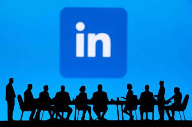 SUNNYVALE, ABD, 10 Ekim 2024 LinkedIn Kurumsal Gelişim Zirvesi. Üst düzey yönetimin siluetleri bir konferans masasının etrafında beyin fırtınası yapıyor. Finansal grafikler arka planda büyük bir ekranda..