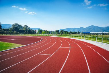 8 şeritli Kırmızı Pist ile modern bir Atletizm Stadyumu manzarası, Canlı Yeşil Araziler ve Serene Doğal Manzarası ile çevrili