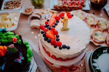 Taze böğürtlenlerle süslenmiş canlı meyveli kekin yakın çekimi ve '1' kek süsü bir çocuğun hayatının ilk yılını simgeliyor.