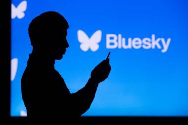 Bluesky 'nin Sosyal Platformunu Keşfeden Genç Asyalı Adam. Akıllı telefondaki genç adamın silueti ve arka plandaki şirket logosu.