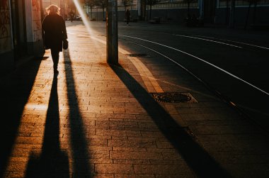 Şehir sokaklarında akşam güneşi altında yürüyen bir yayanın silueti, kentsel hayat çizimi