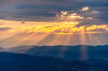 Güneş bulutların arasından parlıyor, güzel bir sahne yaratıyor. Gökyüzü mavi ve turuncu karışımıdır.