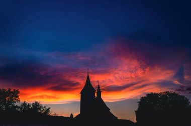 Bir kilise kulesi güzel bir günbatımına karşı siluetlidir. Gökyüzü turuncu ve mor renklerin karışımıdır.