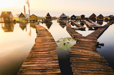 Bir su kütlesinin üzerinde tahta bir köprü. Köprü bir dizi evin ortasında.