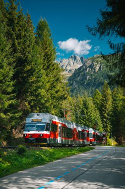 Dağların ihtişamının Slovak seyahatlerinin ebedi cazibesiyle buluştuğu Strbske Pleso 'ya doğru yükselen yüksek Tatras' ın altındaki dağ raylarından kırmızı bir tren geçiyor..
