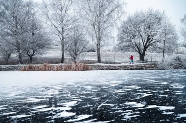 A solitary figure trudges along the snow-covered shore of the frozen lake, enveloped by the cold, silent, and desolate white winter landscape