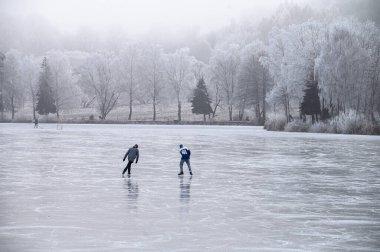 Romantic snowy meadows and frosted trees surround the frozen pond where children find joy in Christmas skating.
