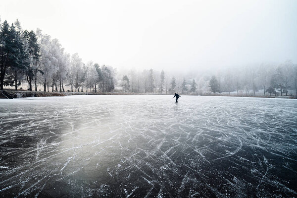Winter fun unfolds as a lone child skates across the icy pond, practicing hockey under a snowy sky