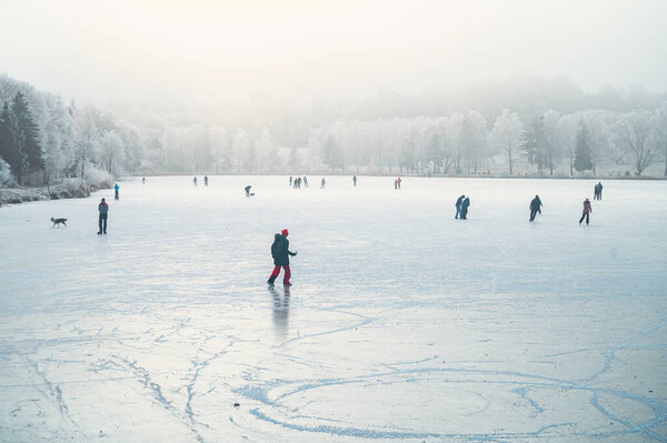 A Christmas tale unfolds on the frozen pond where children skate, embraced by a soft white snowy winter landscape