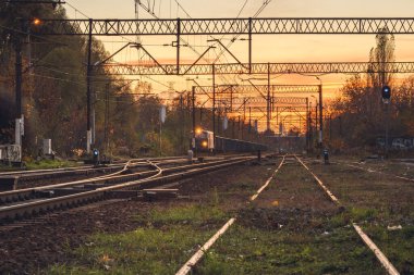 Yük treni yan tarafta duruyor ve gün batımında demiryolu güzergahının görüntüsü için kalkış izni bekliyor..