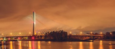 Wroclaw, Odra nehri üzerindeki Redzinski köprüsü, şehrin üzerinde alçak bulutlarla aydınlatılmış bir yapı. Nehrin üzerinden kıyıya bak..