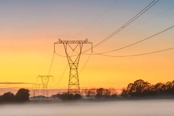 Linia Energetyczna Późnym Wieczorem Mgliste Pole Pomarańczowe Niebo Zachodzie Słońca — Zdjęcie stockowe