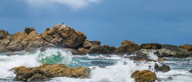 Kıyıdaki mavi sudan çıkan kayalar, güneşli bir yaz gününde kayalara çarpan dalgalar..