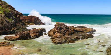 Sahilde volkanik kayalar olan Avustralya kıyıları, deniz kenarındaki kayalıklardan manzara. Şiddetli köpüklü su rüzgarlı havada, dalgalar kayalarda kırılıyor.