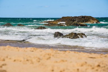 Sahilde volkanik kayalar olan Avustralya kıyıları, plajdan ufka mavi su ve kayalıklarda kırılan dalgalar, yaz güneşli bir gün.