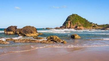 Sahilde volkanik kayalar olan Avustralya kıyıları, plajdan ufka kadar manzara, güneşli bir yaz gününde dalgalı mavi suyla.