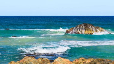 Kıyıdaki mavi sulardan sarkan volkanik kayalar, güneşli bir yaz gününde deniz manzarası..