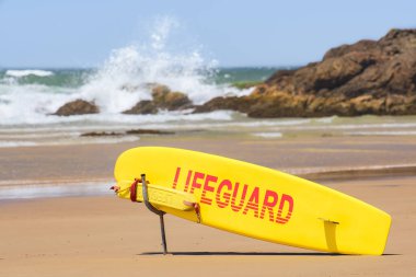 Avustralya kıyıları, kıyıda sarı cankurtaran sörf tahtası güneşli bir yaz gününde kumlu ve kayalık sahillerle korunan şehir plajı.