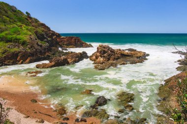 Sahilde volkanik kayalar olan Avustralya kıyıları, deniz kenarındaki kayalıklardan manzara. Şiddetli köpüklü su rüzgarlı havada, dalgalar kayalarda kırılıyor.