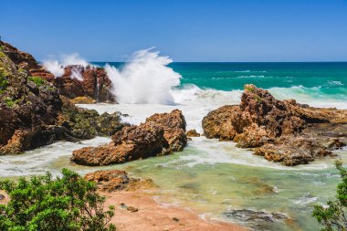 Sahilde volkanik kayalar olan Avustralya kıyıları, deniz kenarındaki kayalıklardan manzara. Şiddetli köpüklü su rüzgarlı havada, dalgalar kayalarda kırılıyor.