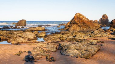 Sahilde volkanik kayaları olan Avustralya kıyıları, sahilden ufka kadar manzarası olan bir yaz akşamı dalgalı mavi su..