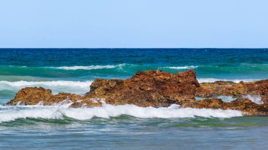 Sahilde volkanik kayalar olan Avustralya kıyıları, plajdan ufka mavi su ve kayalıklarda kırılan dalgalar, yaz güneşli bir gün.