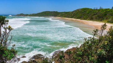 Sahil boyunca uzun bir plajı olan Avustralya kıyıları, deniz kenarındaki bir uçurumdan manzaralı. Rüzgarlı havada güçlü köpüklü su.