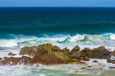Sahilde volkanik kayalar olan Avustralya kıyıları, plajdan ufka mavi su ve kayalıklarda kırılan dalgalar, yaz güneşli bir gün.