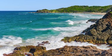 Sahilde volkanik kayalar olan Avustralya kıyıları, plajdan ufka mavi su ve kayalıklarda kırılan dalgalar, yaz güneşli bir gün.
