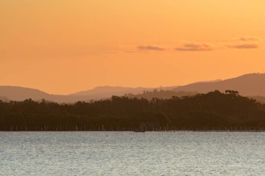 Nehrin üzerinde turuncu gün batımı, uzaktaki aydınlık dağlar..