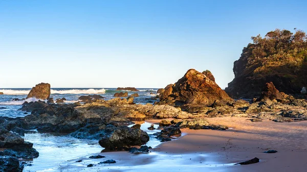 Sahilde volkanik kayaları olan Avustralya kıyıları, sahilden ufka kadar manzarası olan bir yaz akşamı dalgalı mavi su..