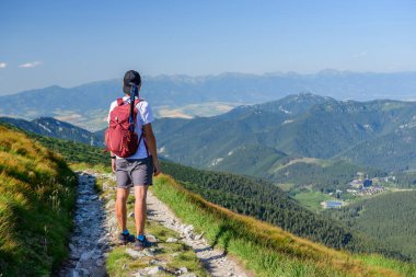 Polonya Tatra Dağları, şortlu genç bir adam ve dağ sırt çantalı bir şapka bir dağ yolunda duruyor ve güneşli bir yaz gününde dağın zirveleriyle vadiyi seyrediyor..