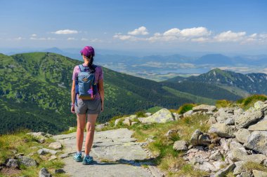 Polonya Tatra Dağları, şortlu genç bir kadın ve dağ sırt çantalı bir şapka bir dağ yolunda duruyor ve güneşli bir yaz gününde dağın zirveleriyle vadiyi seyrediyor..