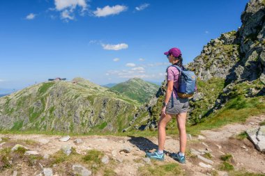 Polonya Tatra Dağları, şortlu genç bir kadın ve dağ sırt çantalı bir şapka bir dağ yolunda duruyor ve güneşli bir yaz gününde dağın zirveleriyle vadiyi seyrediyor..
