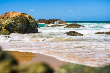 Sahilde volkanik kayalar olan Avustralya kıyıları, plajdan ufka kadar manzara, güneşli bir yaz gününde dalgalı mavi suyla.