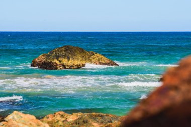 Kıyıdaki mavi sulardan sarkan volkanik kayalar, güneşli bir yaz gününde deniz manzarası..