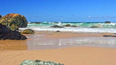 Sahilde volkanik kayalar olan Avustralya kıyıları, plajdan ufka kadar manzara, güneşli bir yaz gününde dalgalı mavi suyla.