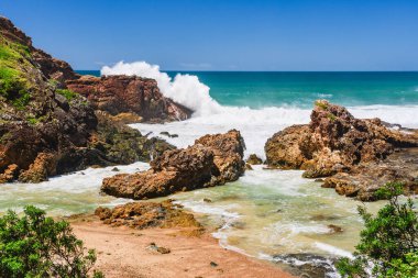 Sahilde volkanik kayalar olan Avustralya kıyıları, deniz kenarındaki kayalıklardan manzara. Şiddetli köpüklü su rüzgarlı havada, dalgalar kayalarda kırılıyor.
