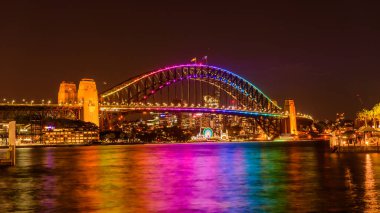 Sydney, Avustralya - 04 Mart 2023: Sydney Limanı Köprüsü gece renkli ışıkla aydınlatılmış, Circular Quay manzaralı.