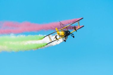 Leszno, Polonya - 22 Haziran 2024: Antidotum Airshow Leszno, İskandinav Hava Gösterisi Pisti, Grumman G-164A Ag-Cat. Uçan bir uçağın kanatlarında akrobatlar gösteri yapıyor, uçağın arkasında renkli dumanlar.