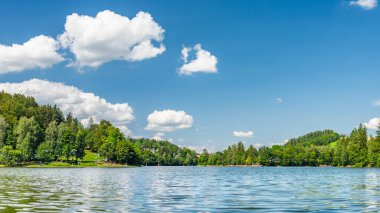 Pastviny Pond, kıyıda yeşil tepeleri olan berrak su. Yaz tatili ve su sporları için popüler bir yer, deniz manzarası..