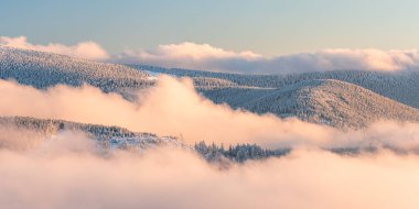 Eastern Sudetes, View of snowy mountain range in fog from hiking trail during winter hike in mountains, viewpoint of wide winter landscape in mountains at sunset. clipart